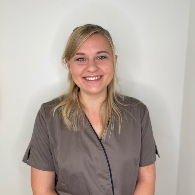 Man sieht eine Mitarbeiterin von Hairfree & Aesthetics auf diesem Bild. Eine zierliche blonde Frau, die angenehm lächelt.